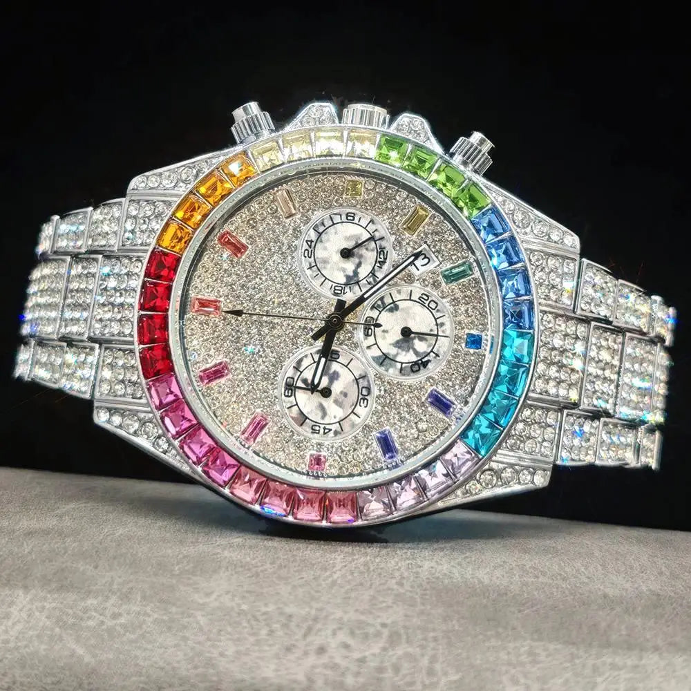 A luxury watch with a silver-tone case and bracelet, heavily embellished with clear crystals. The bezel features a vibrant rainbow gradient of colored crystals, and the dial has three sub-dials with a textured silver face.