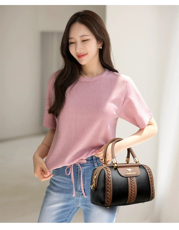 Woman holding a black and brown handbag wearing a pink shirt and blue jeans.