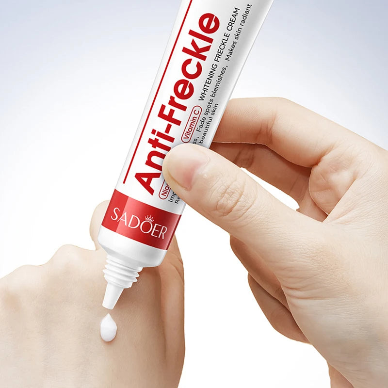 Hand holding a tube of Sadoer Anti-Freckle cream with a small amount on the skin.
