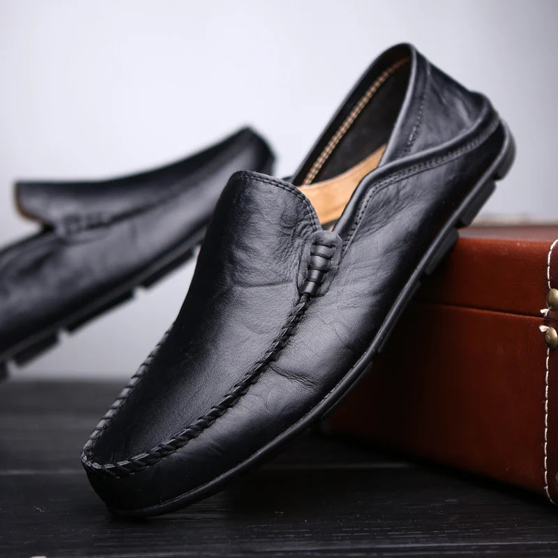 Black leather loafer shoes on a wooden surface with a brown box in the background.