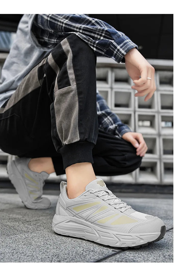 A person crouching outdoors wearing light gray athletic sneakers with pale yellow accents, black jogger-style pants with gray side panels, and a blue plaid shirt.