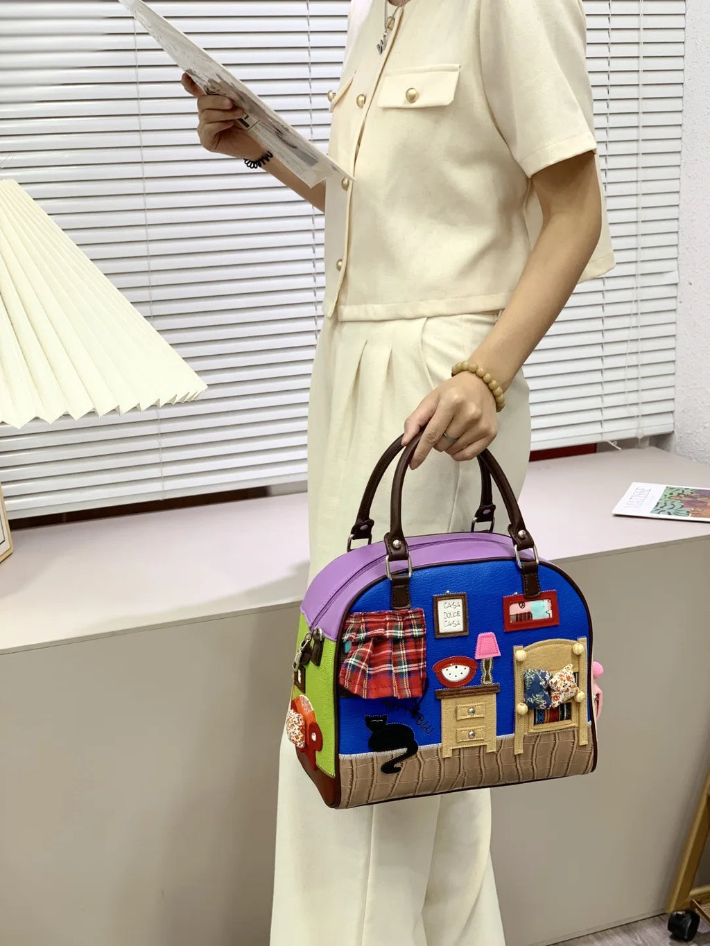 Person holding a colorful handbag with a house design in an indoor setting
