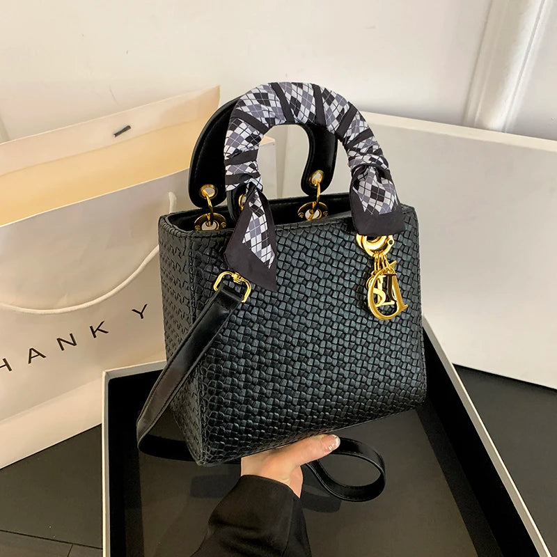 Black handbag with gold accents held by a hand, with a 'Dior' branded box in the background.