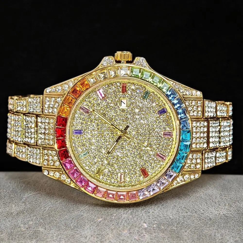 A gold-tone wristwatch with a heavily paved crystal dial and a bezel accented by rainbow-colored crystals, displayed on a gray textured surface against a black background.