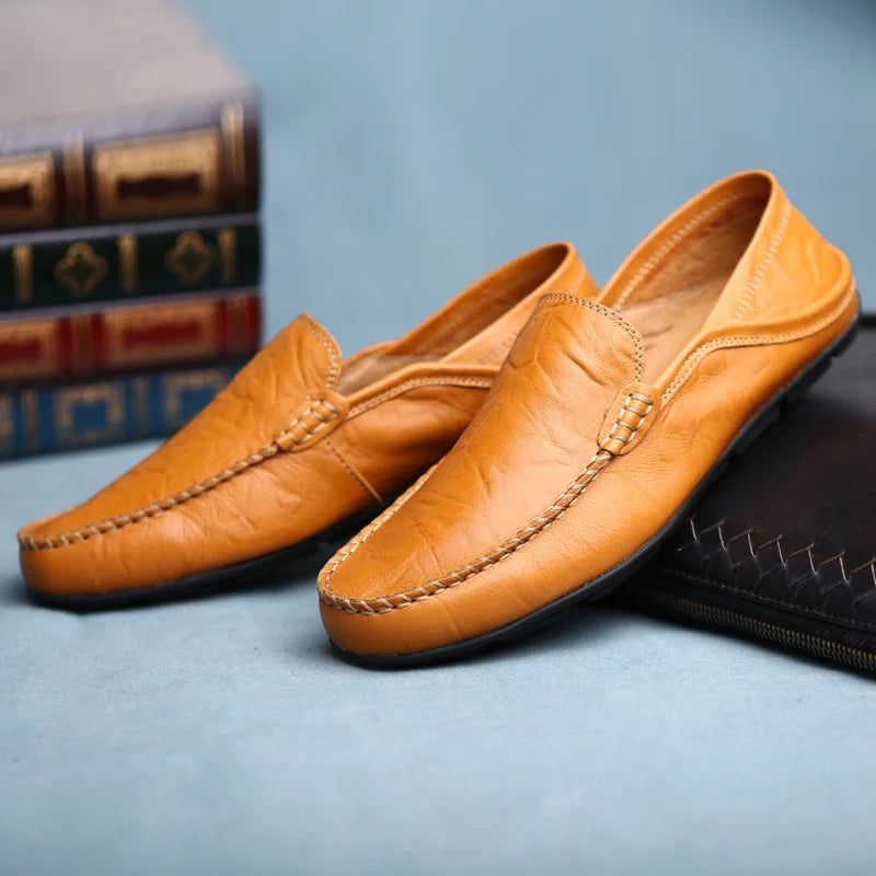 Pair of brown leather loafers on a light blue surface with books in the background.
