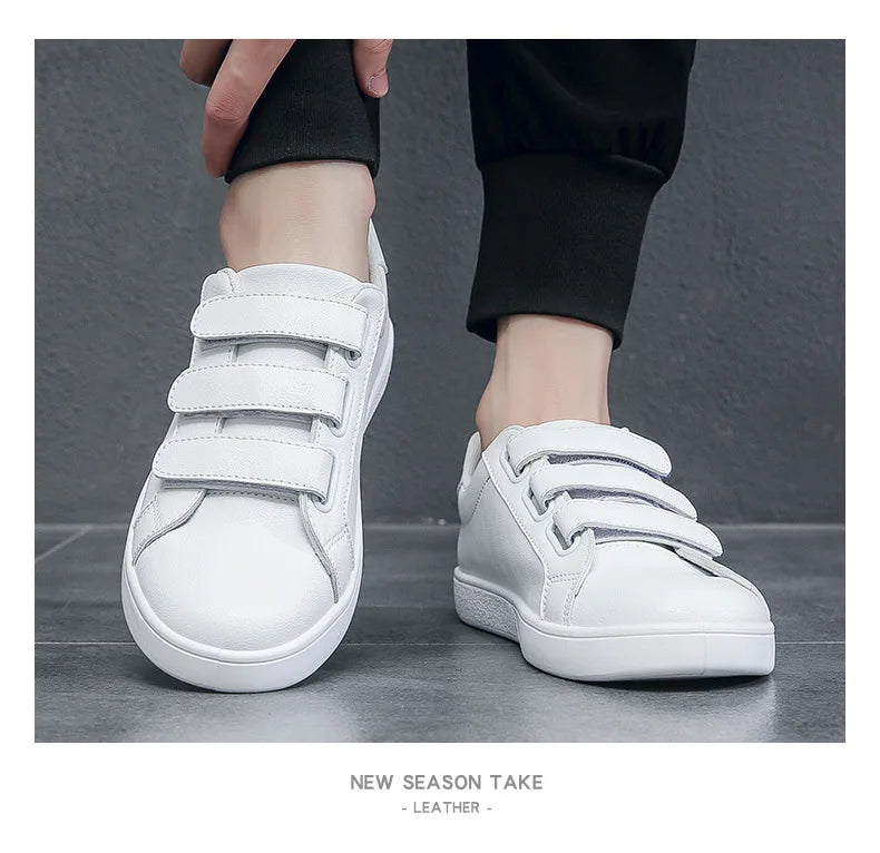 White sneakers with velcro straps worn by a person on a gray background