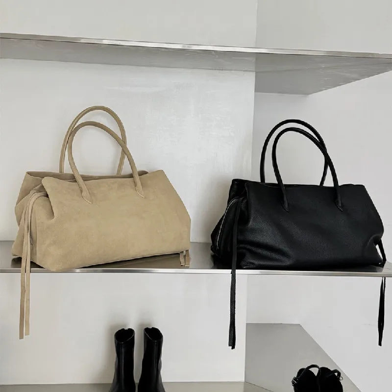 Two handbags, one beige and one black, on a white shelf with a minimal background.