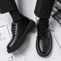 Black leather shoes worn with black pants on a white surface.
