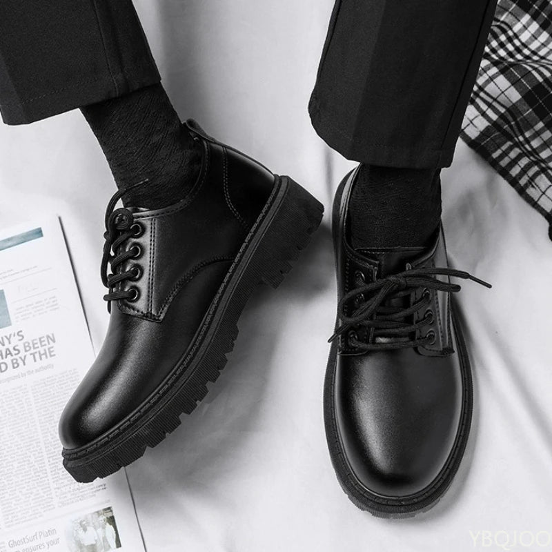 Black leather shoes worn with black pants on a white surface.