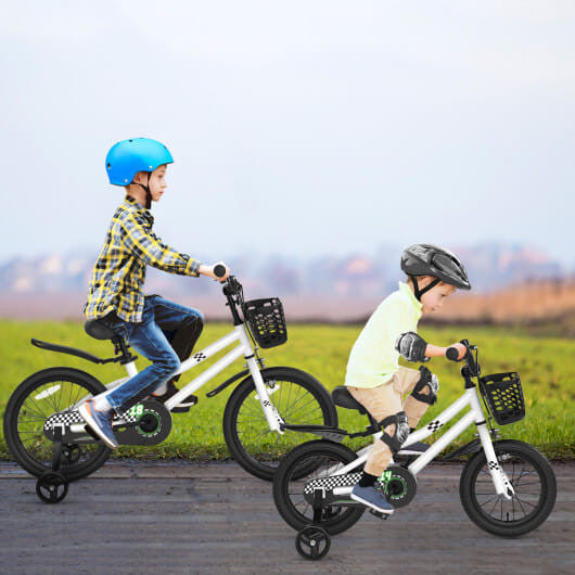 Two children riding white balance bikes with training wheels on a road with a grassy field and sky in the background.