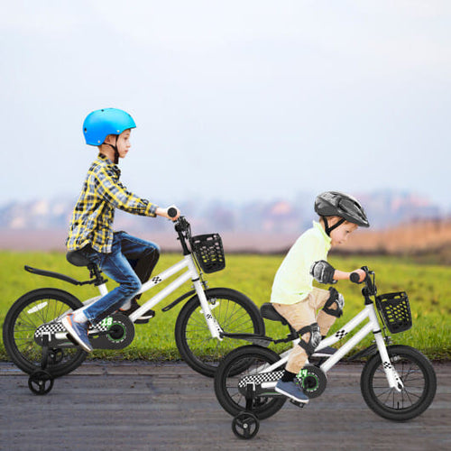 Two children riding white balance bikes with training wheels on a road with a grassy field and sky in the background.