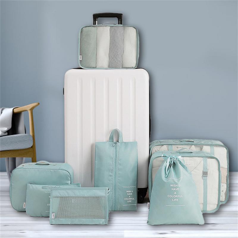 Set of green packing cubes and a white suitcase on a wooden floor with a gray wall background.