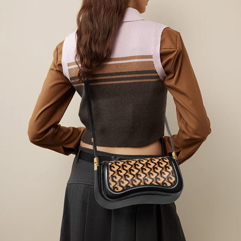 A woman shown from the back wearing a brown long-sleeve top with a light pink and dark brown striped ribbed vest, carrying a black crossbody bag with a tan and black monogram pattern.