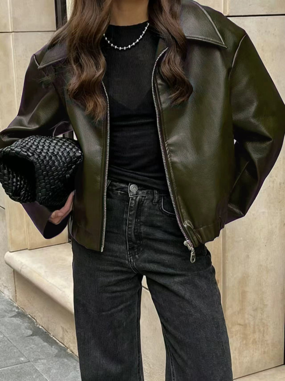 Person wearing a green leather jacket and black outfit holding a black clutch.