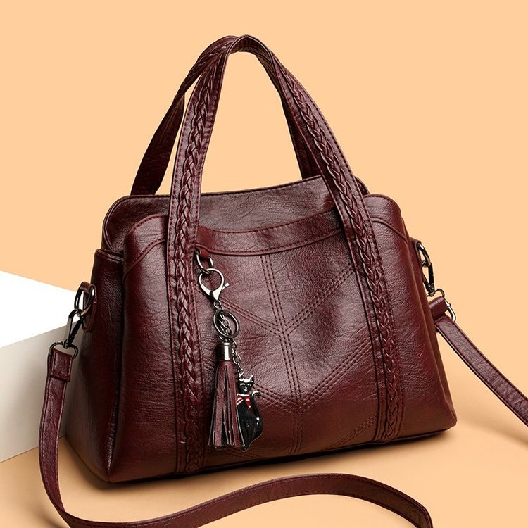 Brown leather handbag with braided handle and keychain on a beige background