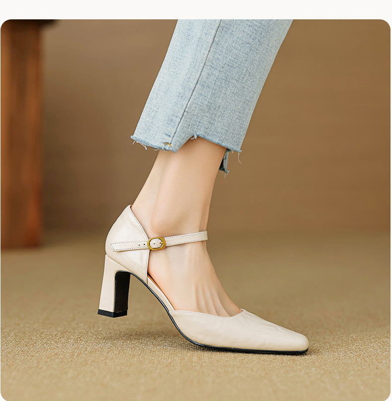 A woman's foot wearing a light beige Mary Jane high heel shoe with a block heel and ankle strap, paired with light blue frayed-hem jeans against a warm brown background.