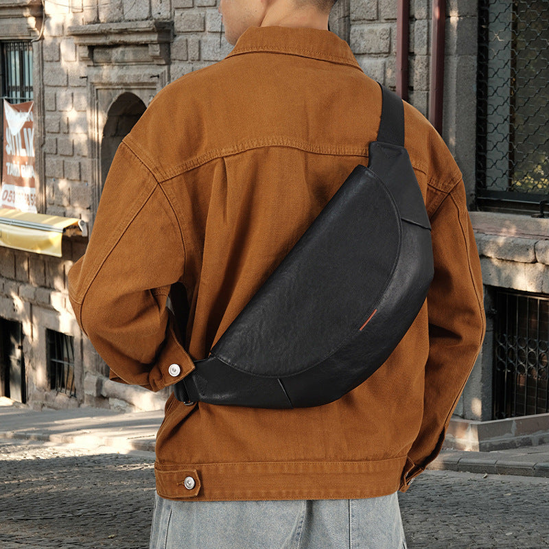 Person wearing a brown jacket with a black sling bag on a stone-paved street.