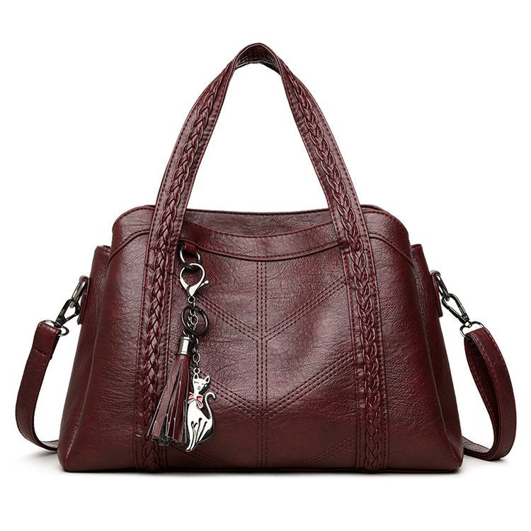 Brown leather handbag with braided handle and cat-shaped keychain on a white background