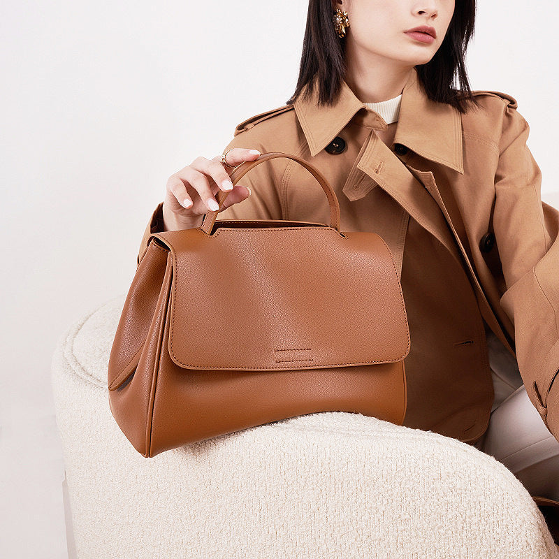 Woman holding a brown leather handbag against a neutral background