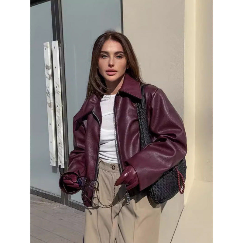 Woman wearing a purple leather jacket and beige pants standing outdoors.