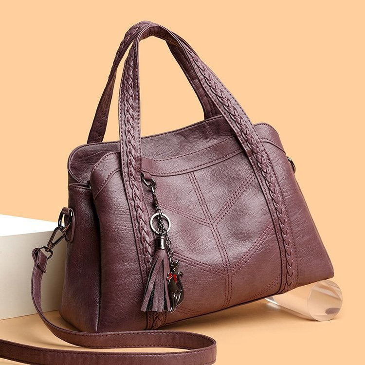 Brown leather handbag with braided handle and tassel on a beige background